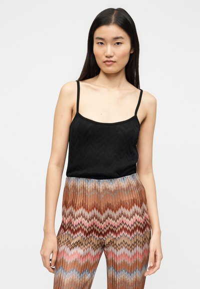 Débardeur noir à fines bretelles avec un motif en zigzag texturé, associé à un pantalon large à motifs chevrons multicolores.