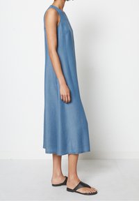 Vestido de mezclilla sin mangas con un escote redondo, corte holgado y longitud a media pantorrilla. La tela es suave, de color azul claro y con costuras sutiles.