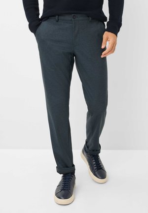 Pantalons bleu canard en tissu lisse, avec une fermeture à bouton et des poches latérales, associés à des baskets bleu marine et des poignets roulés.