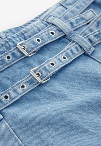 Lichtblauwe denimstof met een aansluitende tailleband, voorzien van zilverkleurige hardware, twee gespen en meerdere oogjes voor aanpassing.