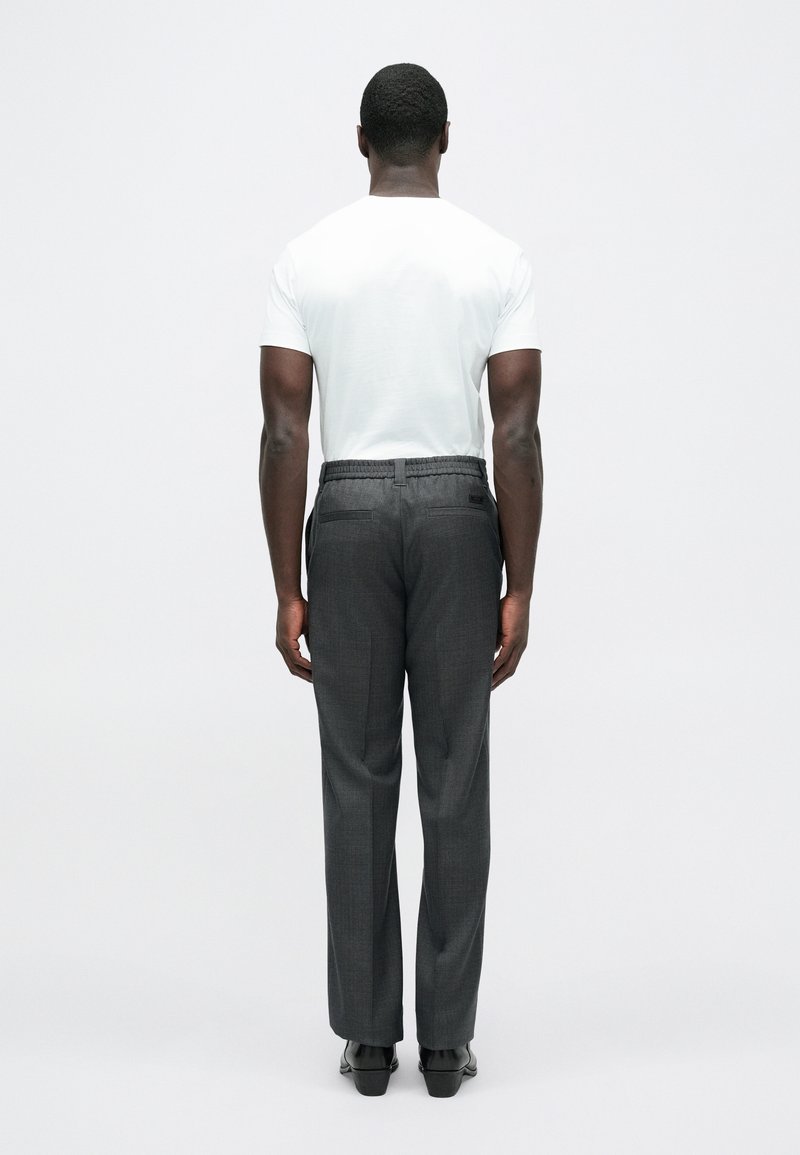 Witte korte mouwen t-shirt gecombineerd met grijze geruite broek, voorzien van een ontspannen pasvorm en zijzakken, gezien van achteren.