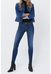 Denim jacket in medium wash blue with front pockets, paired with dark blue skinny jeans and black heeled ankle boots. Smooth texture.