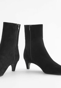 Juodi suede aulinukai iki kulkšnies su siauru kulnu ir šoninėmis užtrauktukais. Lygi tekstūra, kūno formą atitinkantis dizainas ir elegantiška siluetas.