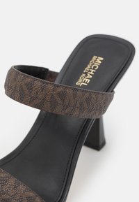 Sandale à talons brune avec une bride texturée arborant un motif de logo. Semelle noire, finition lisse et un solide talon bloc.