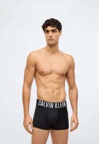 Black cotton boxer briefs with elastic waistband featuring the "CALVIN KLEIN" logo in white. Smooth texture and fitted design.