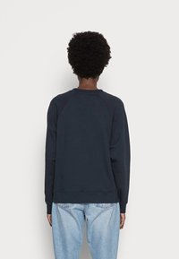 Mörkblå sweatshirt med raglanärmar, ribbade muddar och fåll, tillverkad av ett mjukt material. Bärs med ljusblå jeans vilket ger en avslappnad passform.