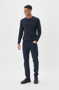 Jūrų pajėgų apvalios kaklo megztinis ir atitinkamos tamsiai mėlynos kelnės, derinamos su juodais slip-on batais. Lygus paviršius, pritaikyta forma, minimalus detalizavimas.