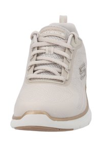 Scarpa sportiva beige con tomaia in rete, design testurizzato, lacci morbidi e un accento dorato sulla suola. Presenta un'etichetta con marchio e suola flessibile.