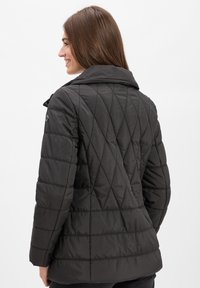 Schwarze, gesteppte Jacke mit hohem Kragen, die diagonale Nähmuster und einen Knopfdetails am Ärmel aufweist. Glattes, glänzendes Material.