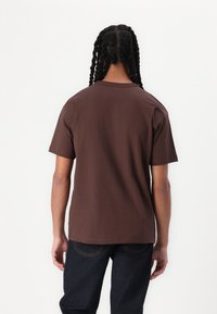 Brun bomulls T-skjorte med korte ermer, rund hals og en avslappet passform. Glatt tekstur og minimalistisk design. Brukt med mørk denimjeans.