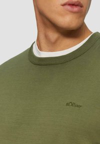 Olivgrüner Pullover mit Rundhalsausschnitt und gerippten Bündchen, mit kleinem s.Oliver-Logo auf der Brust. Weicher, strukturierter Stoff.