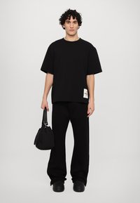 Svart oversized t-skjorte med korte ermer og en sidemerke; parret med løse svarte bukser og en liten svart veske; matte sko.