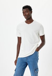Witte t-shirt met korte mouwen en v-hals van een zachte stof, gecombineerd met lichtblauwe cargobroeken met zijzakken.