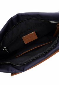 Interno della borsa navy con foderatura in tessuto liscio. Presenta un'etichetta in pelle marrone e una tasca con zip nera per una conservazione sicura.