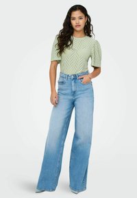 Lys grøn, kortærmet, strikket top med diamantmønster; højtaljede, brede, lys blå denimjeans med en bleget finish.