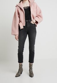 Różowa, teksturowana kurtka z wysokim kołnierzem, czarna bluzka, ciemne dżinsy z wysokim stanem i ankle boots w wzór węża.