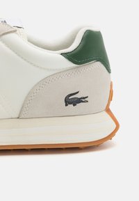 Sneaker in pelle bianca con accento verde sul tallone, pannello in suede beige e logo in cocco nero. Suola in gomma arancione con battistrada.