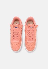 Pink leather sneakers with a perforated toe box, flat laces, and a white outsole. Features a multicolored Nike logo on the side.
