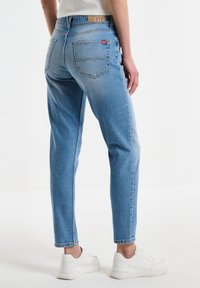 Jeans de mezclilla azul claro con corte recto, que presentan una cintura alta, bolsillos traseros y una etiqueta de marca en la cinturilla.