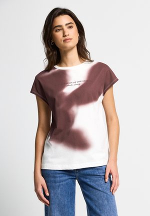 Hvid bomulds T-shirt med maroon tie-dye design i den øverste sektion og teksttryk. Korte ærmer og afslappet pasform, parret med blå denim jeans.