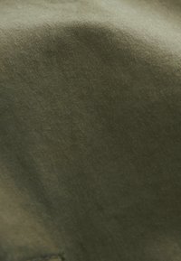 Material de culoare verde măsliniu, cu o suprafață netedă și ușor texturată. Materialul pare durabil, având o culoare solidă, estompată, fără modele vizibile.