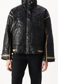Czarna pikowana kurtka puchowa z kwiecistym tłoczeniem, brązowymi akcentami, wysokim kołnierzem, kieszeniami na zamek oraz regulowanym sznurkiem u dołu.