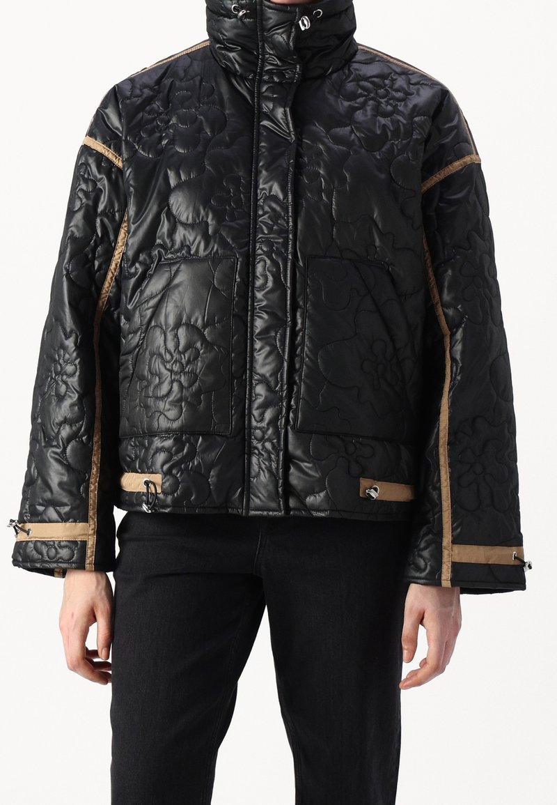 Czarna pikowana kurtka puchowa z kwiecistym tłoczeniem, brązowymi akcentami, wysokim kołnierzem, kieszeniami na zamek oraz regulowanym sznurkiem u dołu.