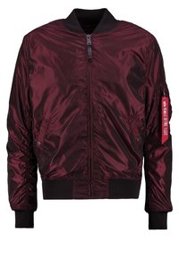 Burgundowa kurtka bomberka z lekkiego satynowego materiału z zamkiem błyskawicznym z przodu, ściągaczami na mankietach i kieszeniami po bokach. Na rękawie znajduje się czerwona metka z tkaniny.