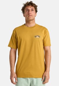 Sennepsgul T-shirt lavet af bomuld med korte ærmer, med en rund halsudskæring og et lille logo-patch på venstre bryst.