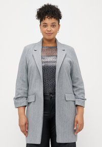 Grijze visgraat blazer met reverskraag, lange mouwen en twee voorzakken, gelaagd over een geblokt topje en gecombineerd met donkere broeken.
