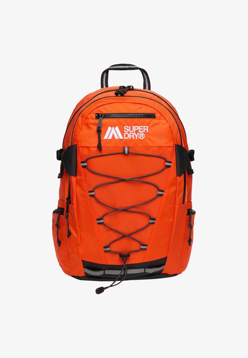 Pomarańczowy plecak nylonowy z czarnymi akcentami, regulowane szelki, przedni design z gumką, wiele kieszeni zamykanych na zamek oraz uchwyt do noszenia na górze.