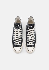 Sapatilhas de cano alto pretas com um padrão salpicado, atacadores brancos e capas de bico em borracha, apresentando um cabedal em lona e detalhes em off-white contrastantes.