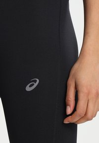 Czarne legginsy wykonane z elastycznego materiału o gładkiej fakturze. Posiadają odblaskowe szare logo po boku oraz dopasowany krój.