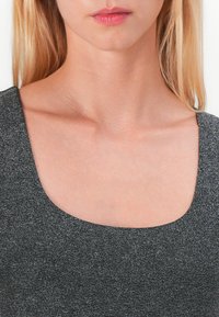 Schwarzes strukturiertes Oberteil mit weitem Rundhalsausschnitt. Das Material hat einen leichten Schimmer und eine glatte Oberfläche, die die Haut knapp unterhalb des Schlüsselbeins zeigt.