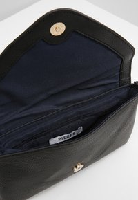 Černá kožená taška s texturovaným povrchem, vybavená zlatým zapínáním na druk a tmavě modrým vnitřkem, který obsahuje kapsu na zip a značkovou etiketu.