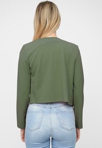 Kort, lange mouwen jack in olijfgroene stof met een gladde textuur. Heeft een ronde halslijn en een gestroomlijnde pasvorm rond de taille.