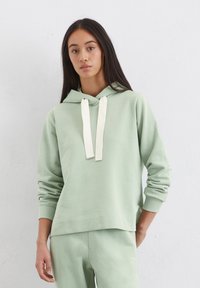 Lichtgroene hoodie van zacht katoen, voorzien van een voorzak en contrasterende crème trekkoorden, gecombineerd met bijpassende joggers.