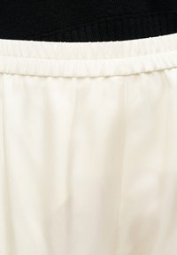 Ceinture élastique blanche avec un tissu ivoire froncé en dessous et un tissu en maille noire au-dessus.