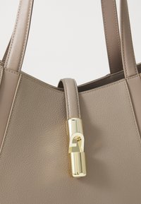 Beige leather tote bag with a textured finish, featuring a gold-tone lock accent and dual flat straps.