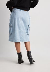 Gonna di jeans di un blu chiaro con tasche laterali cargo, dal taglio dritto e con una vita. Abbinata a stivaletti neri alla caviglia con tacco spesso.