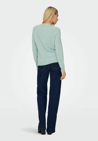 Light green knit sweater with long sleeves, round neckline, and ribbed hem, paired with dark blue straight-leg jeans and black block-heeled shoes.