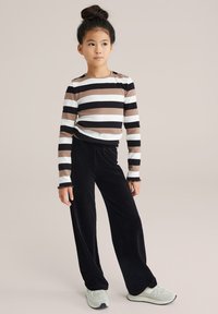 Dlhý rukáv pruhovaná blúzka v hnedej, čiernej a bielej farbe, v kombinácii s čiernymi kordovým nohavicami. Obsahuje vlnité manžety a svetlé tenisky.