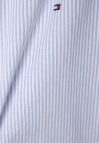 Tela de rayas azules y blancas con una textura suave. Presenta un pequeño logo en rojo, blanco y azul. El diseño es clásico y atemporal.