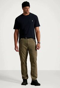 T-shirt azul-marinho com gola redonda combinada com calças cargo oliva. O material parece algodão; as calças possuem vários bolsos e um corte folgado. Ténis pretos.