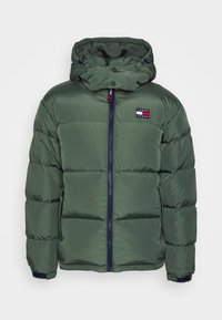 Veste matelassée verte avec fermeture éclair à l'avant, col montant et capuche amovible. Comprend un patch logo et des poignets élastiques pour un ajustement confortable.