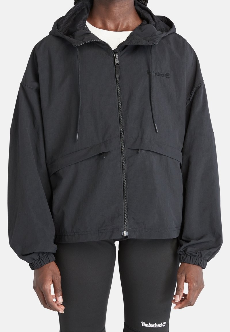 Giacca nera leggera con cerniera frontale, cappuccio regolabile e polsini elasticizzati; presenta un design semplice e lineare senza motivi visibili.