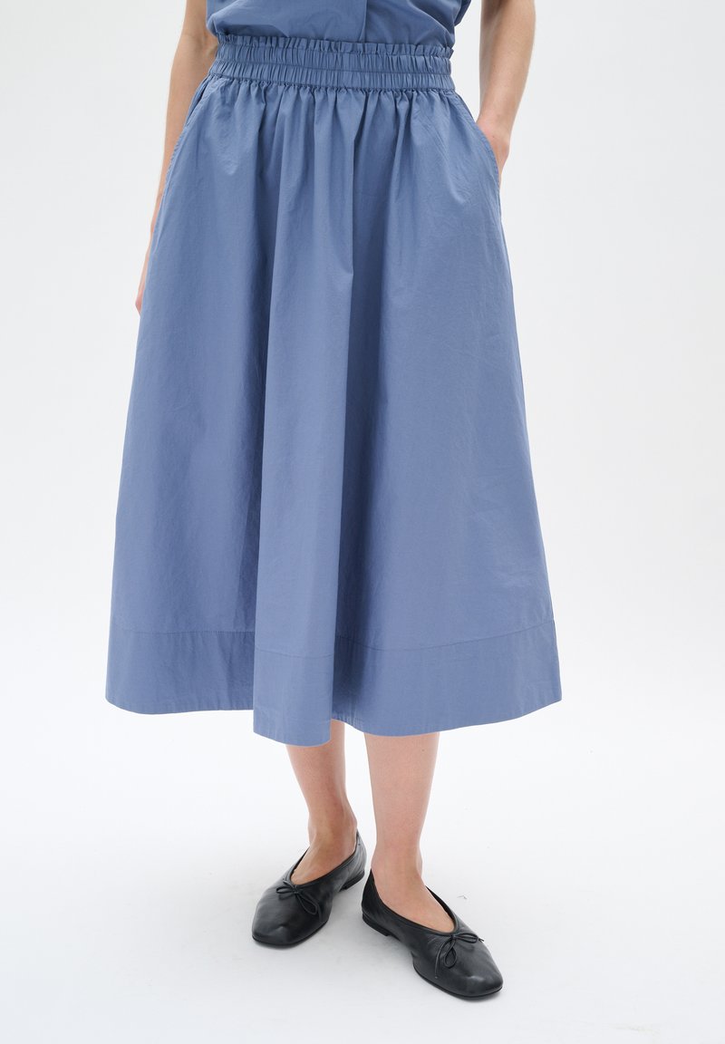 Light blue skirt with a gathered elastic waistband, knee-length, made of lightweight fabric; features side pockets and a smooth texture.