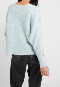 Maglione corto azzurro chiaro con un design a coste testurizzato. Materiale morbido con maniche lunghe. Abbinato a jeans neri a vita alta.