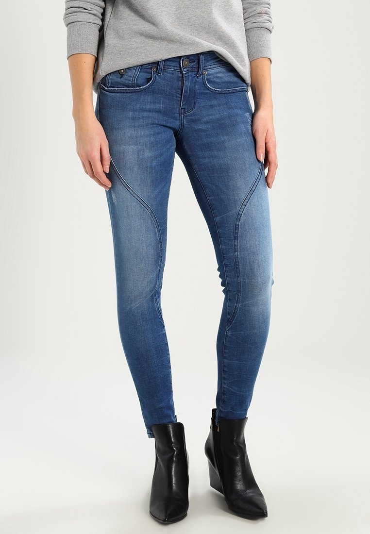 Úzké džíny ve středně modrém denimovém odstínu, s vybledlým umytím, dekorativním šitím a vysokým pasem. V kombinaci s černými kotníkovými botami.