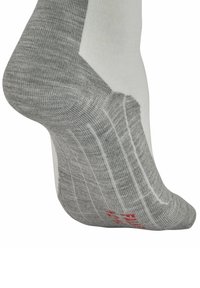 Chaussette de sport grise et blanche avec une texture côtelée, un talon renforcé et un détail de logo rouge sur le dessous. Montre une vue partielle de côté.